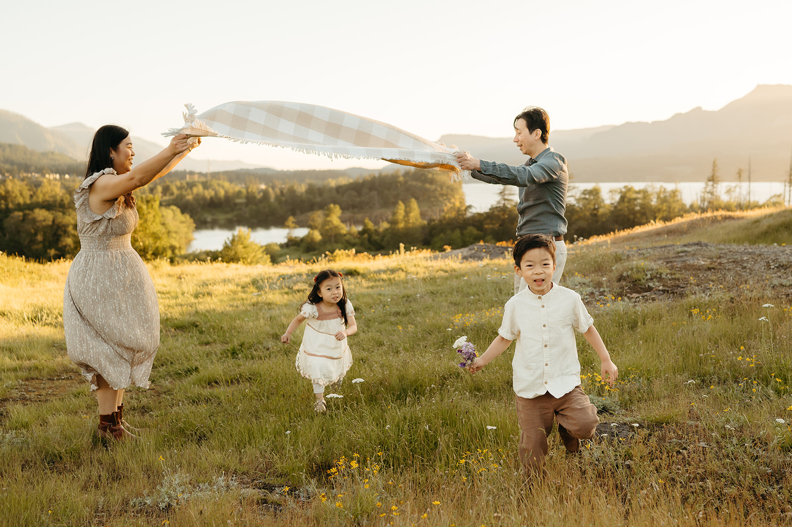 Family playing with a blanket in a wildflower field overlooking the Columbia River Gorge during a golden hour photo session near Portland, Oregon